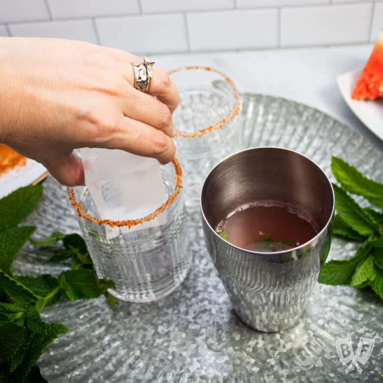 Placing a king cube into a double rocks cocktail glass.