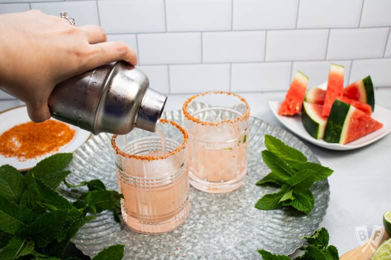 Pouring a watermelon and tequila cocktail into Tajín rimmed cocktail glasses.