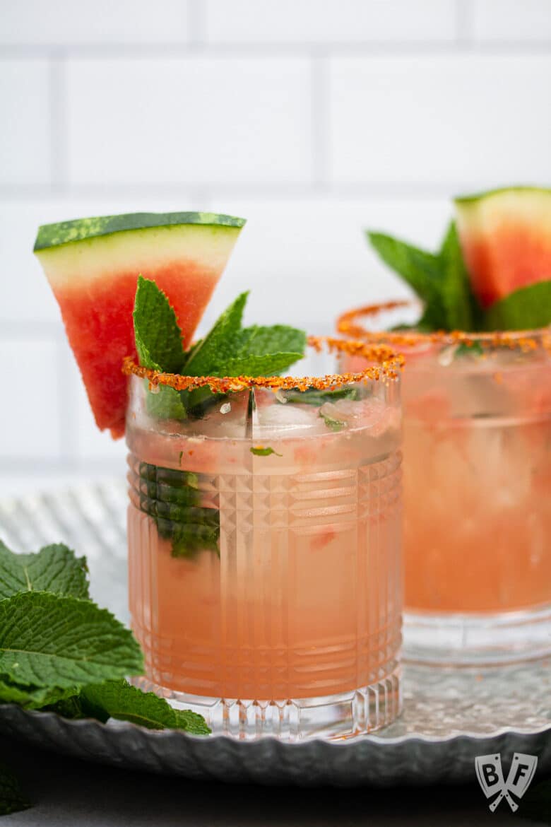 A close-up of 2 watermelon cocktails with mint and Tajin on the rim.