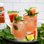 Tray of cocktails made with watermelon, mint, lime, and tequila with a bottle of Tajin seasoning in the background.