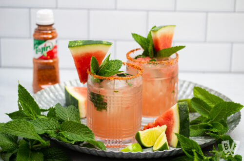 Tray of cocktails made with watermelon, mint, lime, and tequila with a bottle of Tajin seasoning in the background.