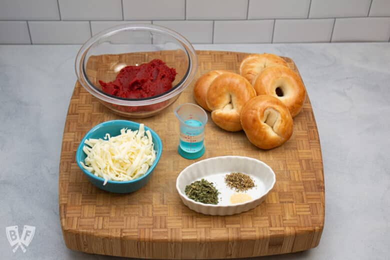 Ingredients for homemade mini pizza bagels on a butcher block.