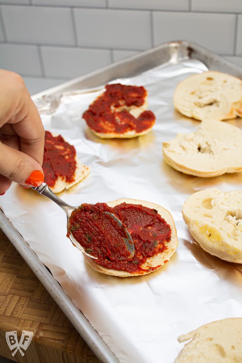 Spreading homemade pizza sauce onto mini bagels.