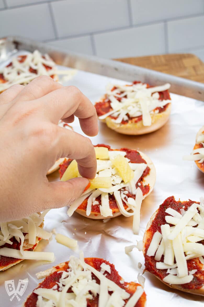 Topping a mini pizza bagel with pineapple.