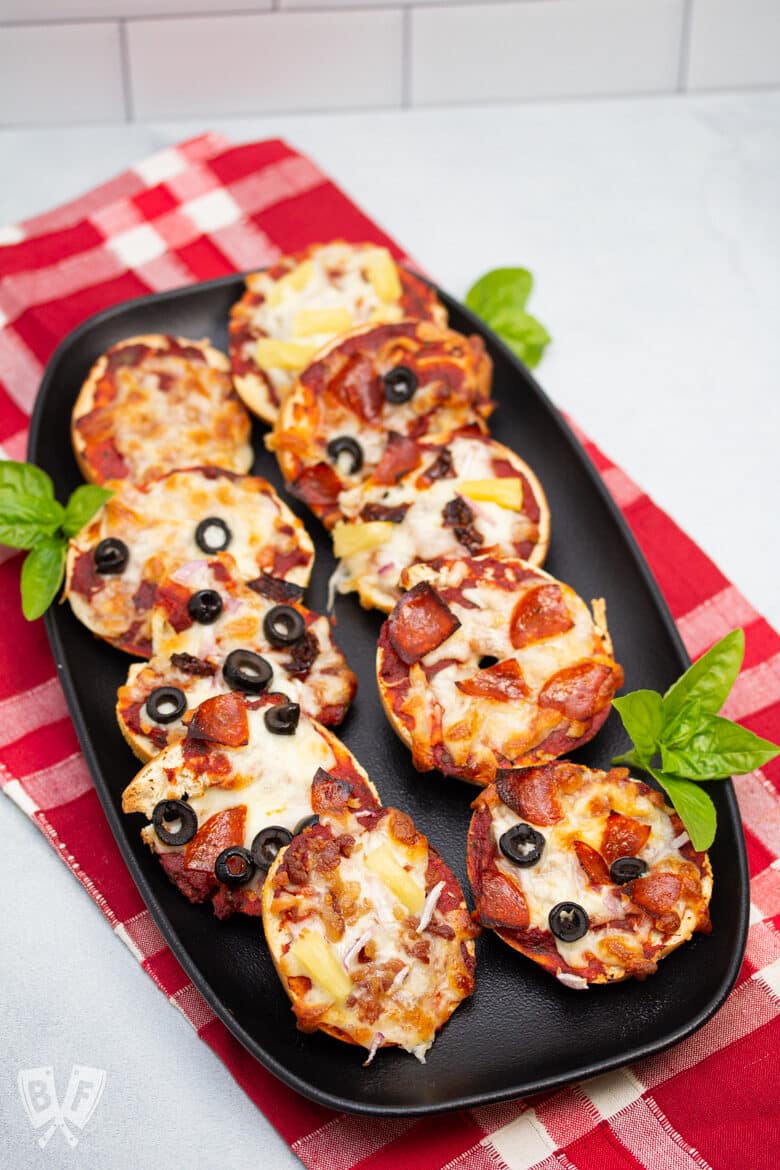 Platter of 10 assorted mini pizza bagels with fresh basil.