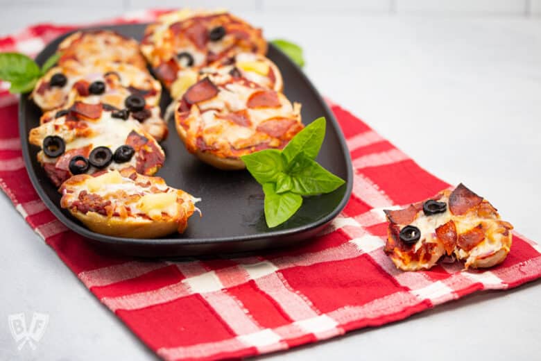 Platter of mini pizza bagels with assorted toppings and fresh basil.