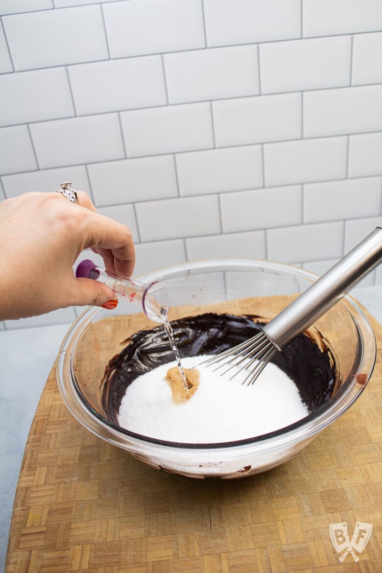 Adding mint extract to a bowl of chocolate, sugar, and vanilla.