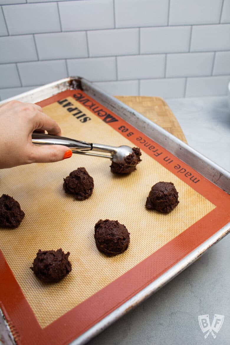 Scooping chocolate cookies onto a prepared baking sheet.