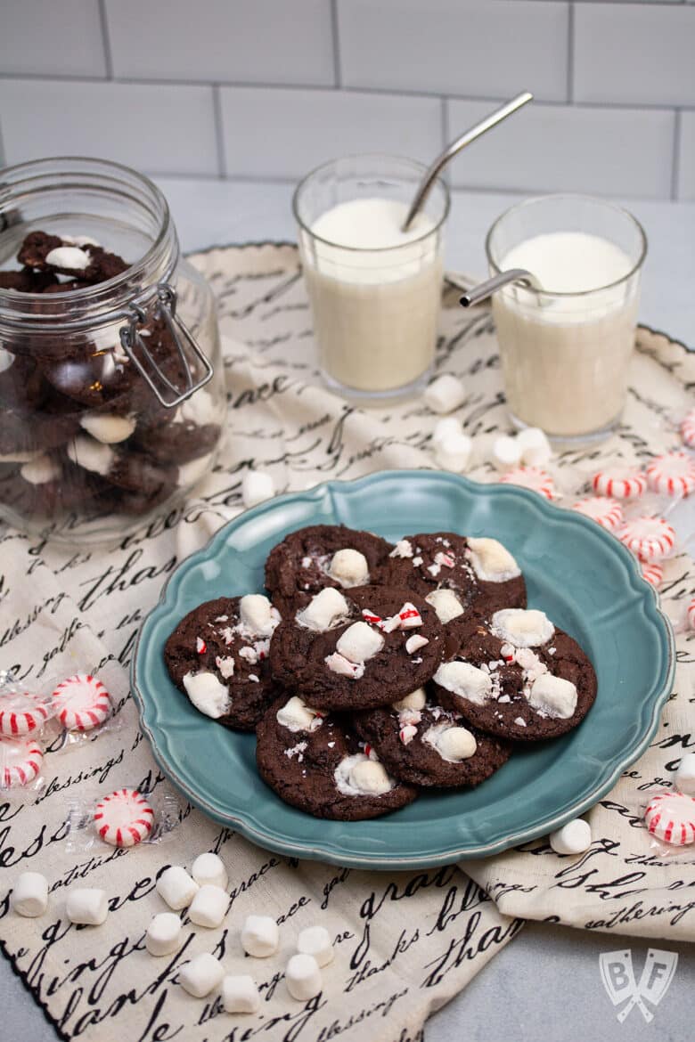 Plate of peppermint hot chocolate cookies with glasses of milk, marshmallows, and peppermints alongside.