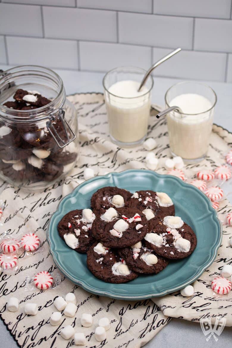 Cookie jar and platter of peppermint hot chocolate cookies with glasses of milk alongside.