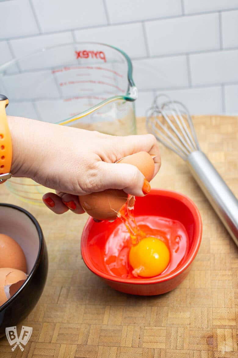 Hand cracking an egg into a small bowl.