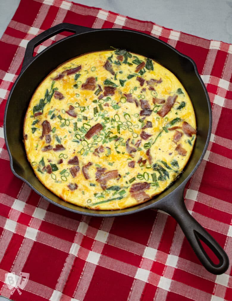 Spinach, bacon, green onion, and cheddar frittata in a cast iron skillet.