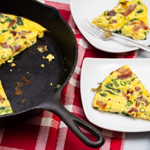 Frittata in a cast iron skillet with a few slices taken out on plates to the side.