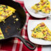 Frittata in a cast iron skillet with a few slices taken out on plates to the side.