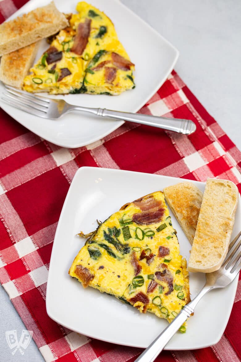 Two wedges of spinach, bacon, green onion, and cheddar frittata with toasted English muffin slices.