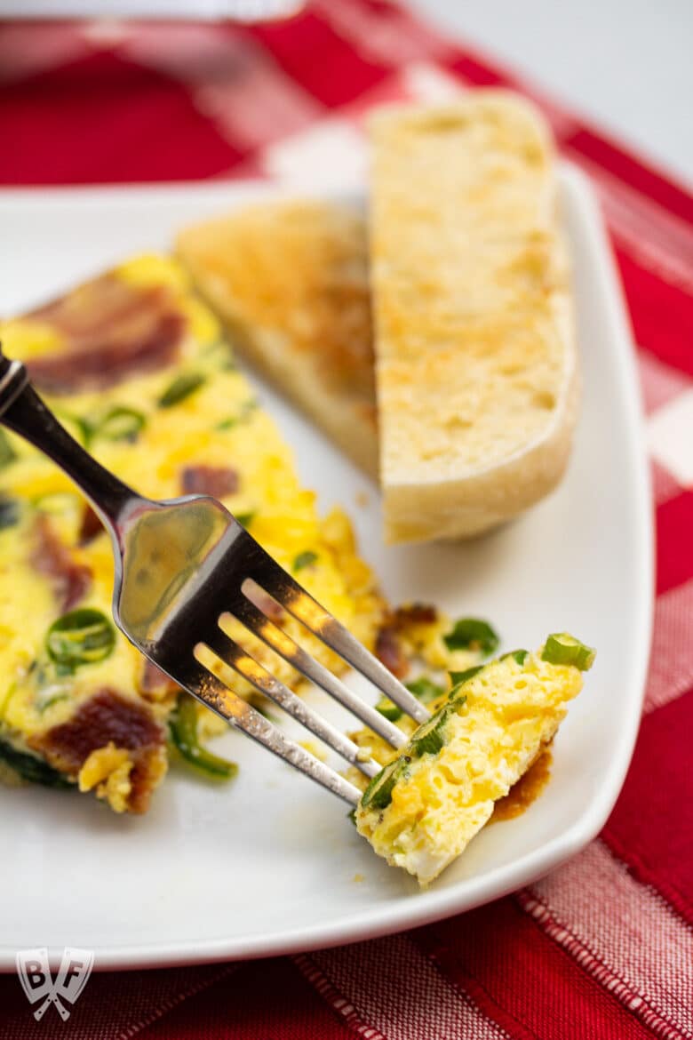 Close-up of a fork taking a piece from a spinach, bacon, green onion, and cheddar frittata.