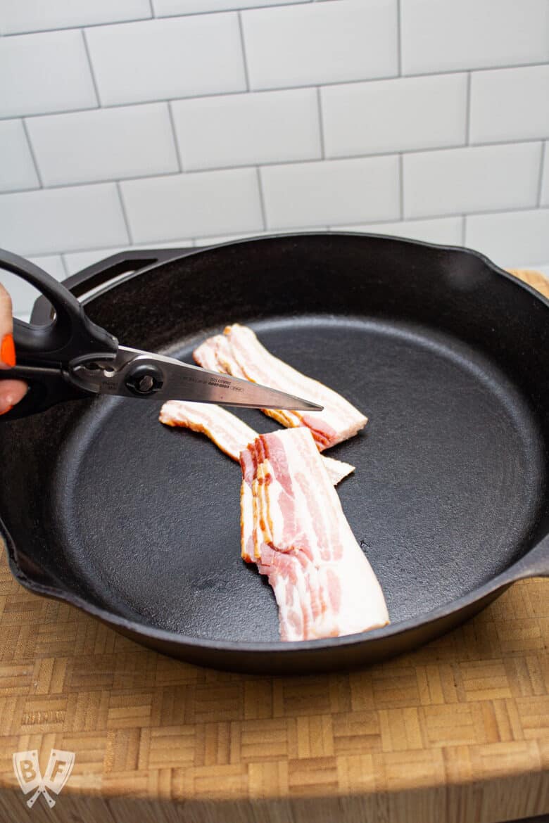 Bacon being cut with kitchen scissors over a cast iron skillet.