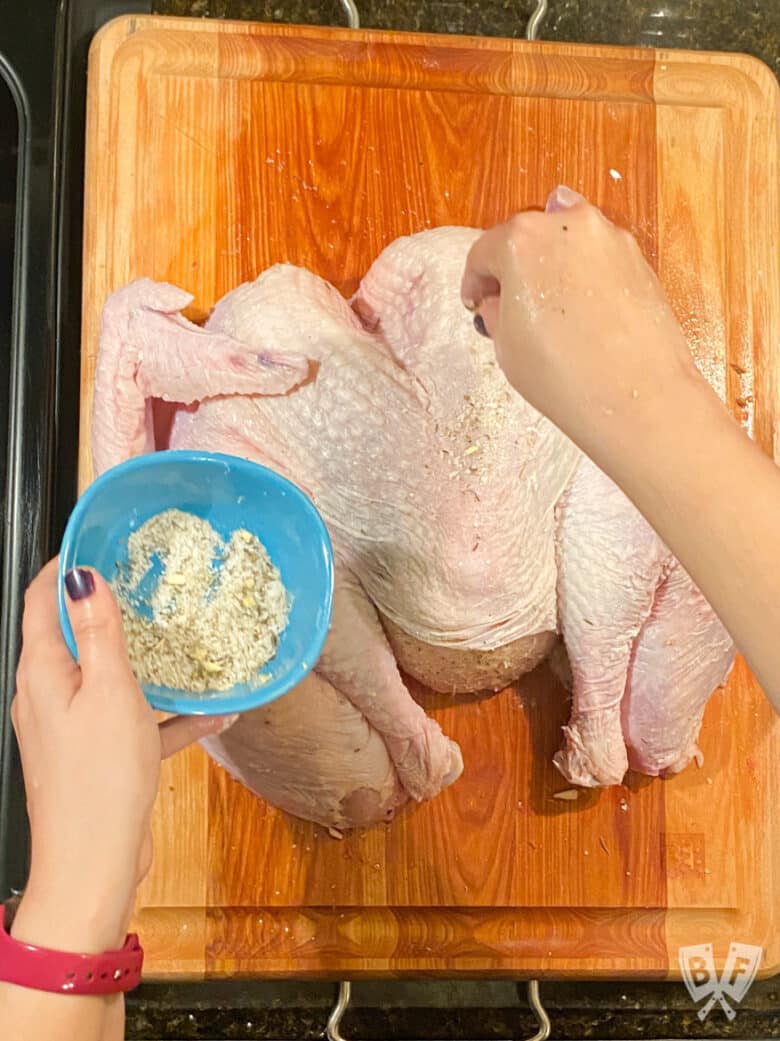 Sprinkling dry brine seasoning blend onto a turkey.