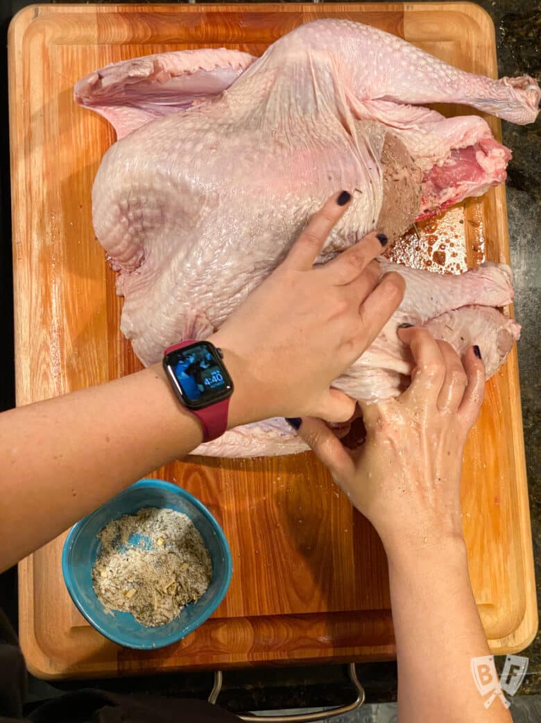 Rubbing dry brine seasoning mix underneath the skin of a spatchcocked turkey.