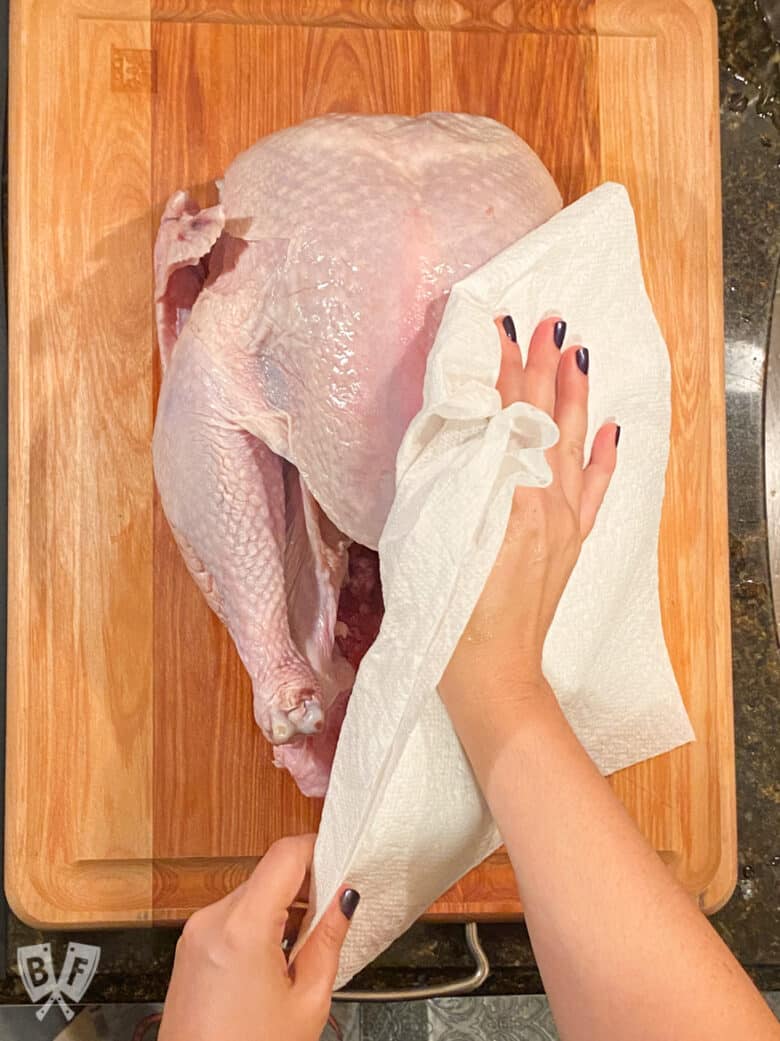 Patting the skin of a raw turkey dry.