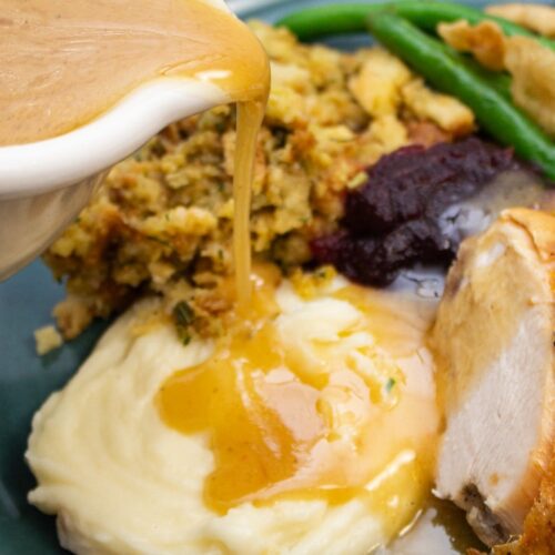 Pouring gravy onto mashed potatoes on a plate of Thanksgiving food.
