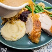 Pouring gravy onto mashed potatoes on a plate of Thanksgiving food.