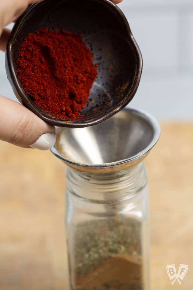 Pouring ground paprika through a funnel into a spice jar.