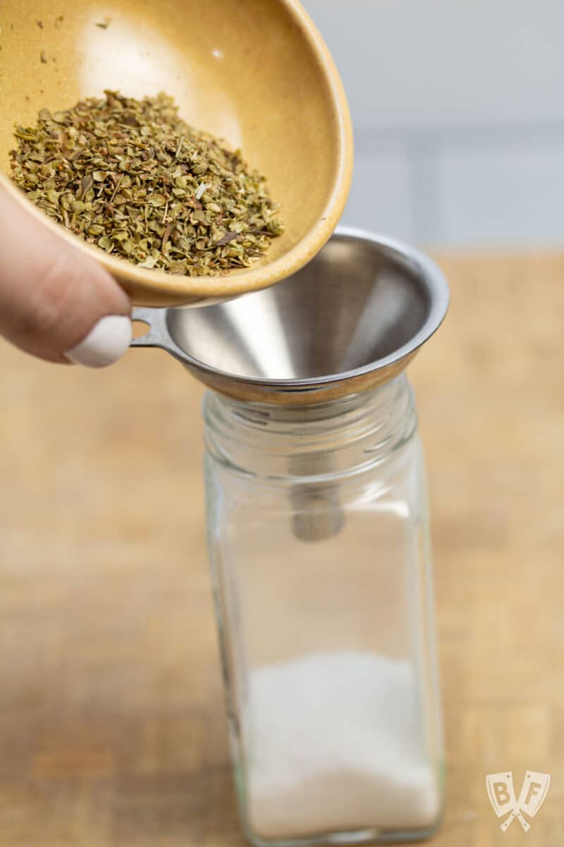 Pouring dried oregano through a funnel into a spice jar.