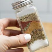 Holding a spice jar with layers of ingredients for homemade fajita seasoning Penzeys copycat recipe.