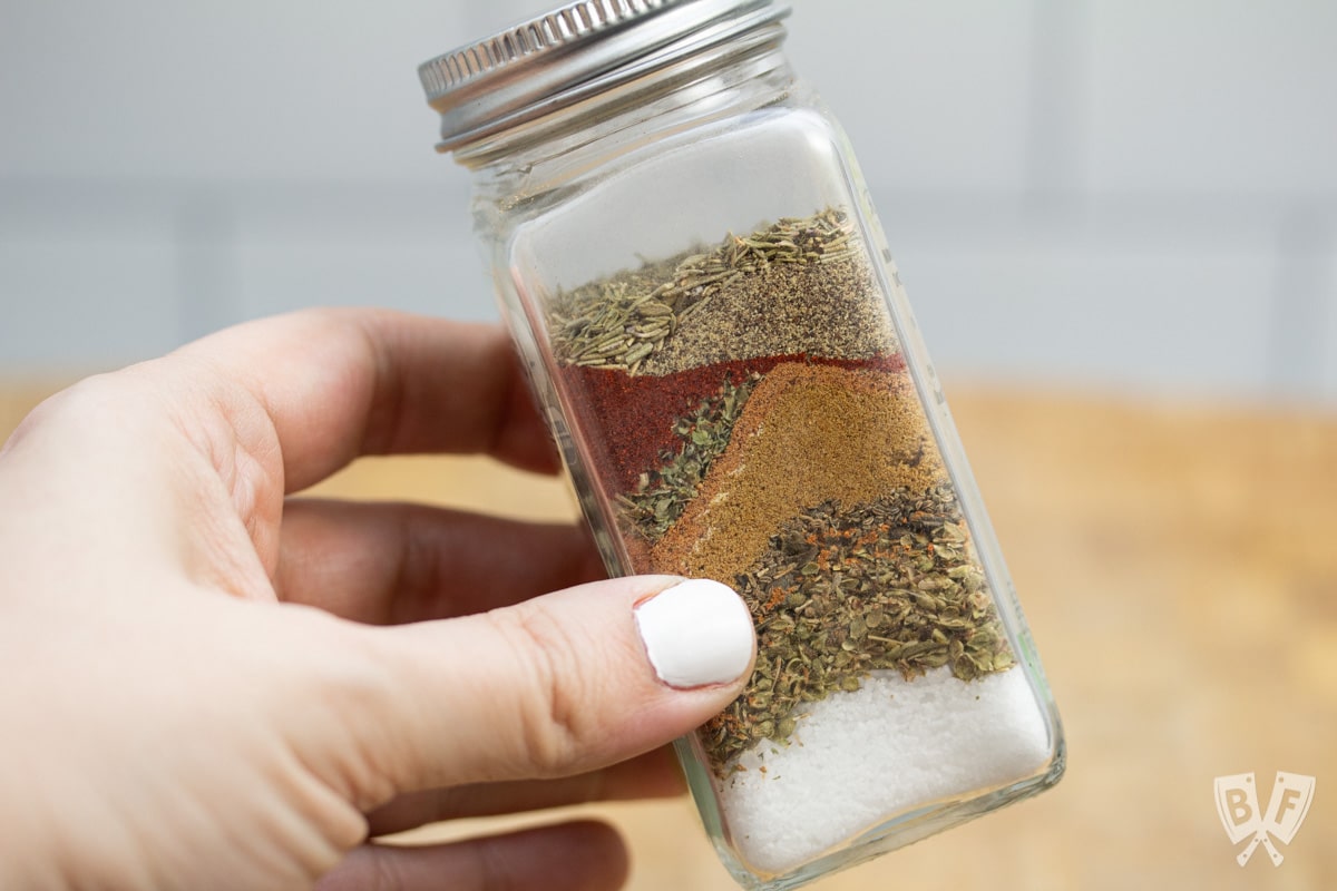 Holding a spice jar with layers of ingredients for homemade fajita seasoning Penzeys copycat recipe.