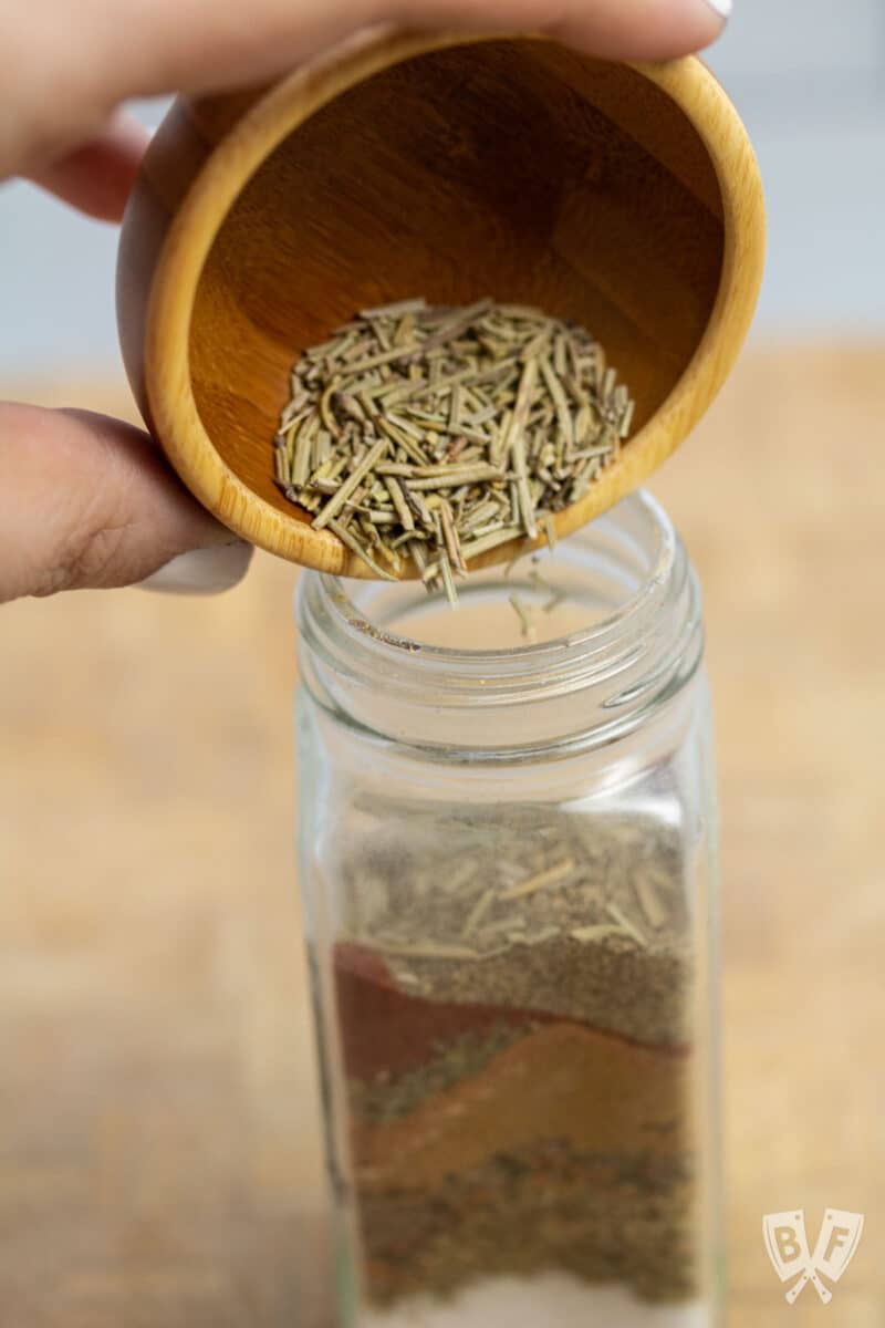 Pouring dried rosemary through a funnel into a spice jar.