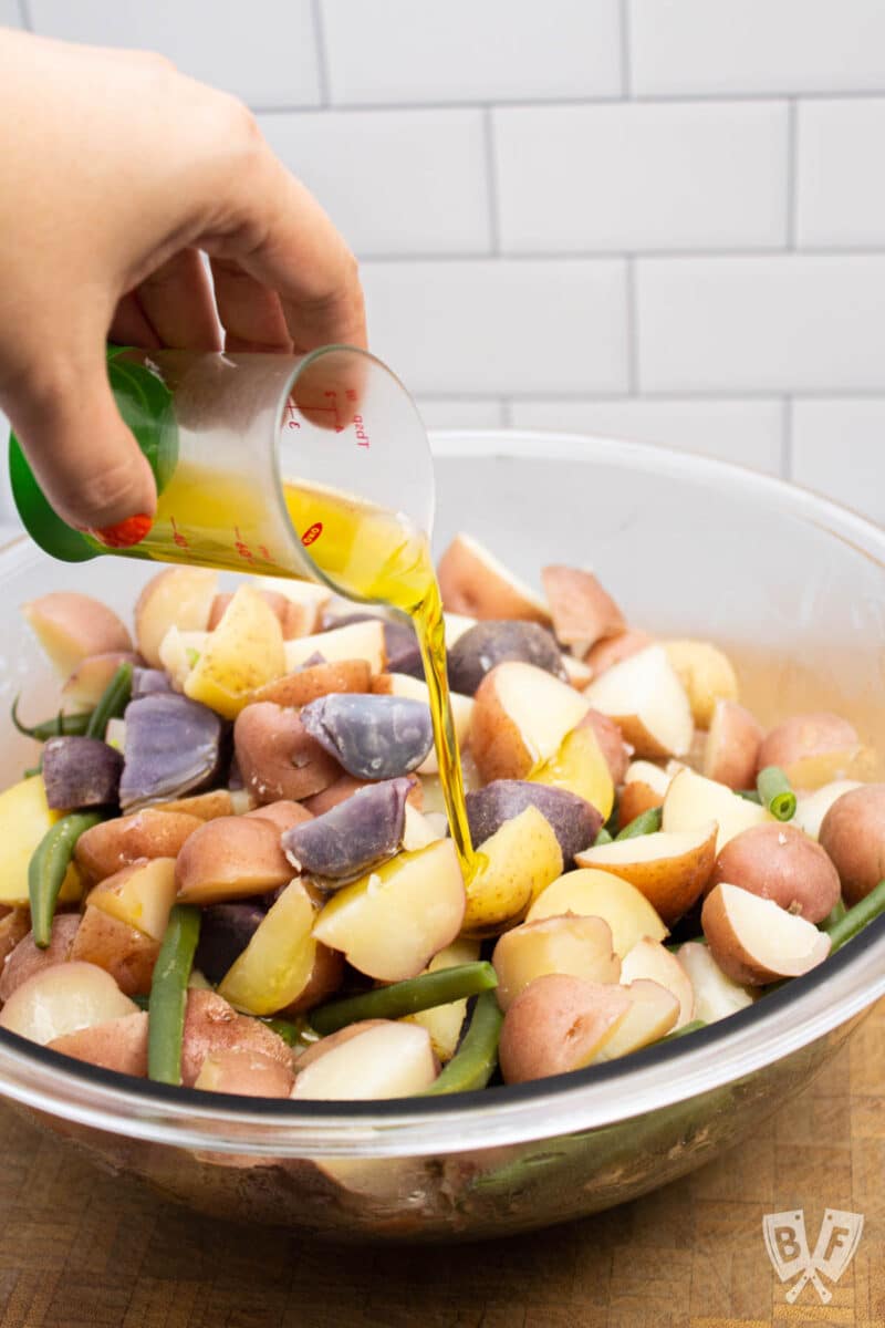 Drizzling olive oil onto a bowl of hot potatoes and green beans.