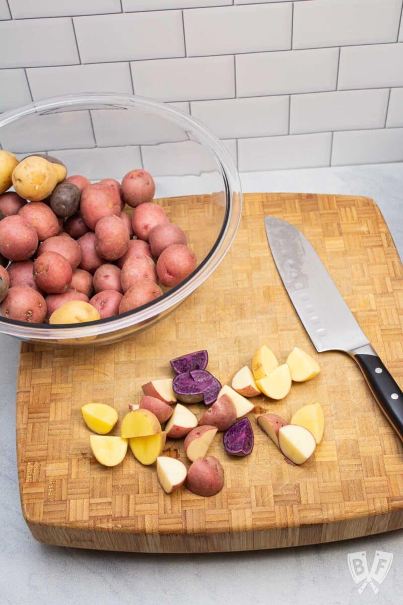 A bowl of multi-colored baby potatoes being cut with a knife.