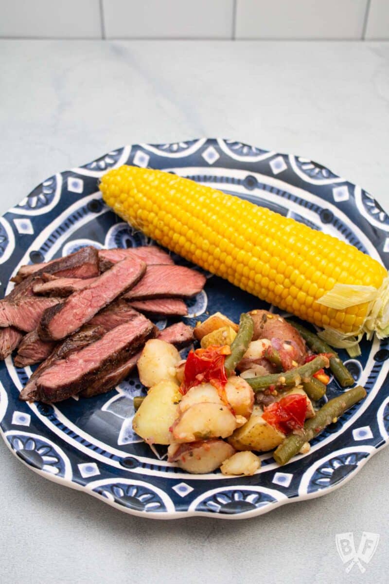 Plate with Calabrese potato salad, sliced steak, and corn on the cob.