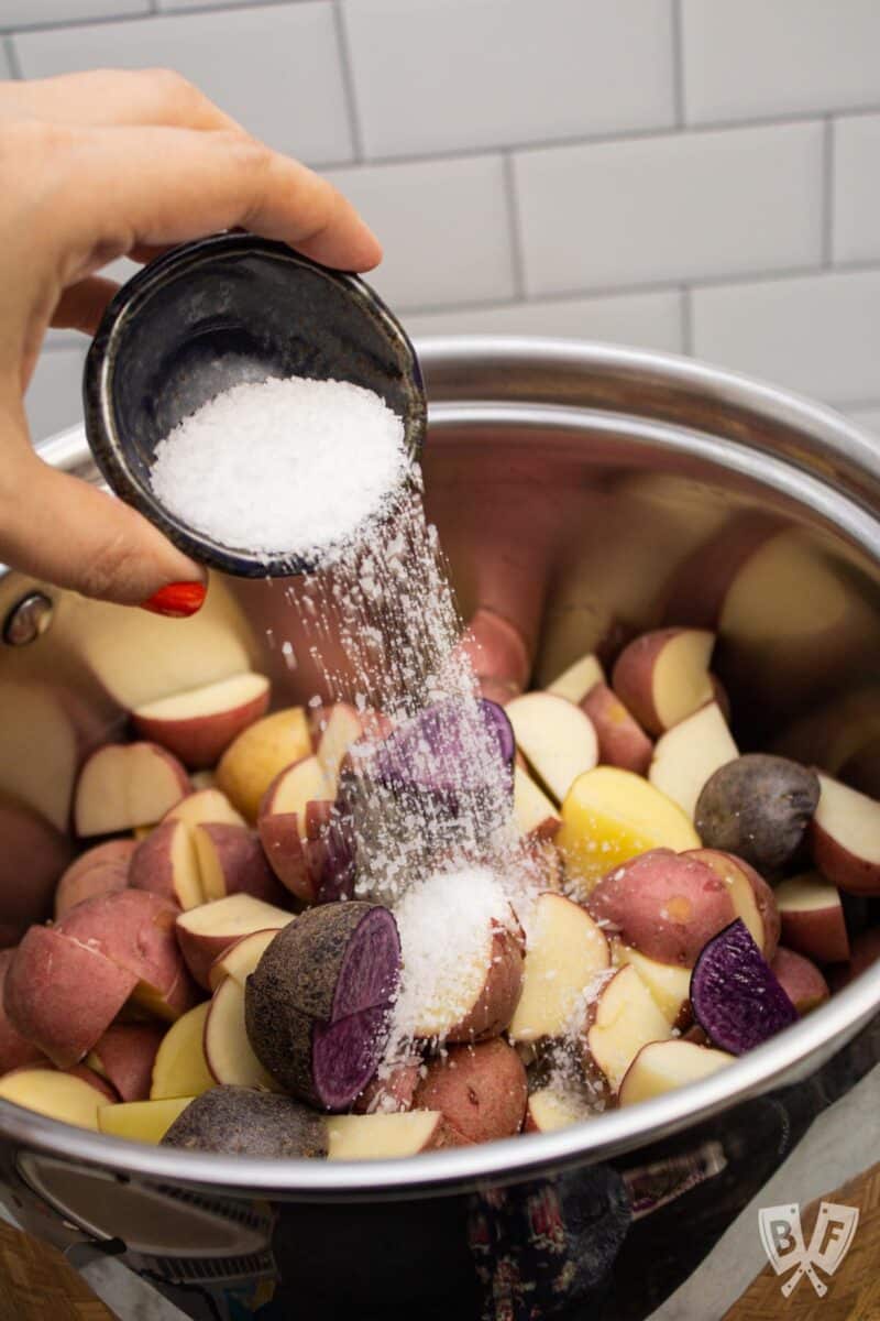 Adding salt to a pot of colorful baby potatoes.