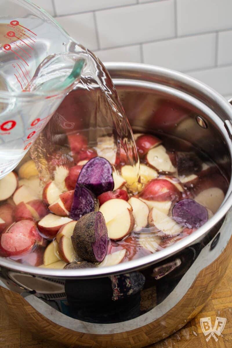 Pouring water into a large pot of raw potatoes.