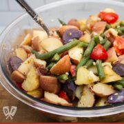 Scooping up Calabrese potato salad with green beans and tomatoes from a bowl.