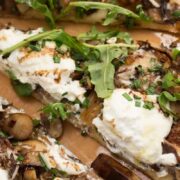 Mushroom and ricotta pizza with baby arugula drizzled with aged balsamic, sliced into triangles.