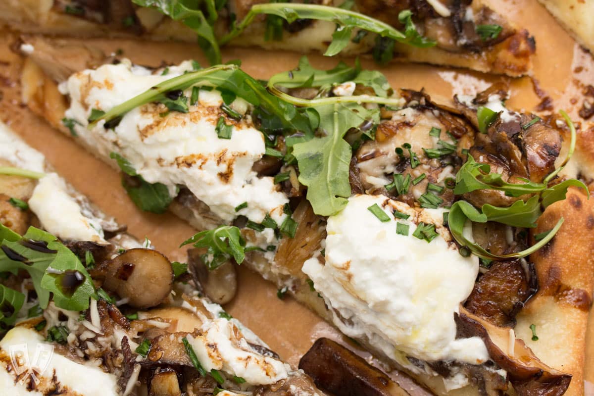 Mushroom and ricotta pizza with baby arugula drizzled with aged balsamic, sliced into triangles.