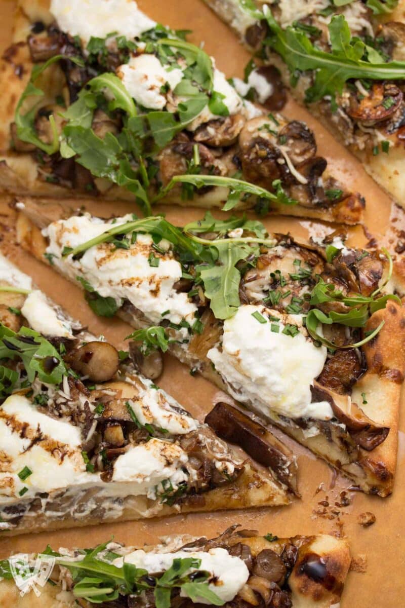 Mushroom pizza sliced into triangles topped with greens and aged balsamic.