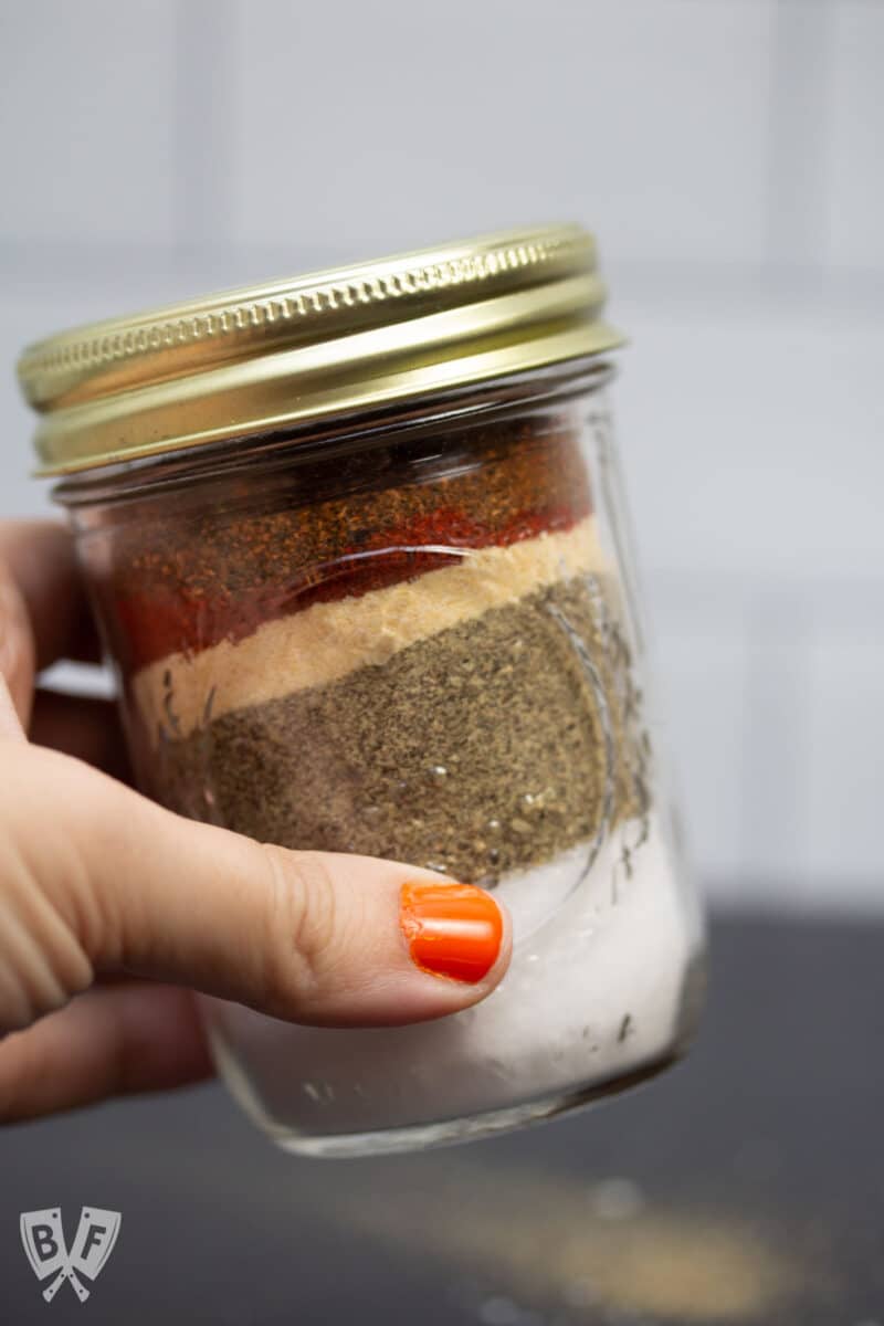 Holding a glass jar filled with layers of spices.