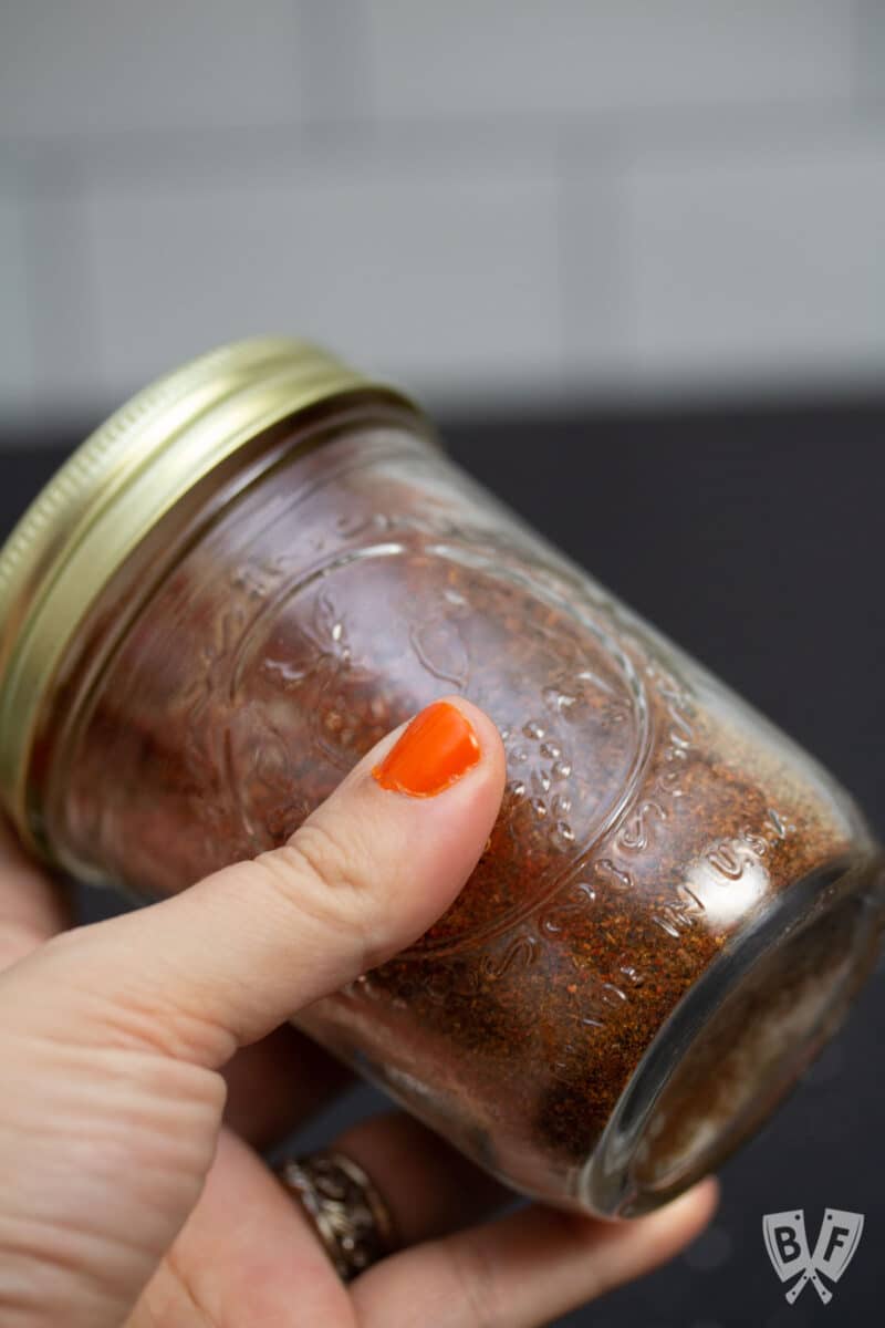 Shaking a glass jar full of spices to combine.