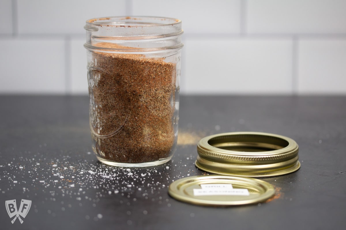 Glass jar with homemade spice mix inside next to a labeled metal lid.