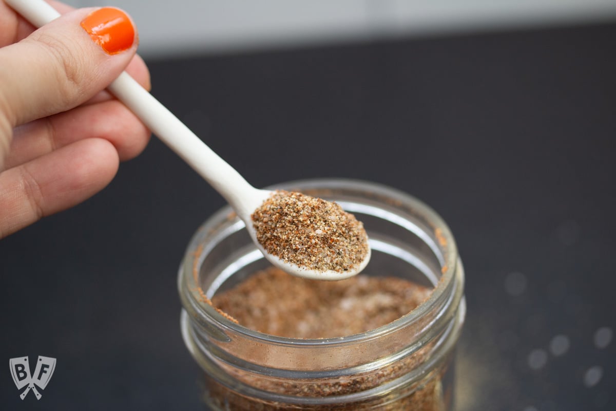 Scooping a small spoonful of homemade grill seasoning from the jar.