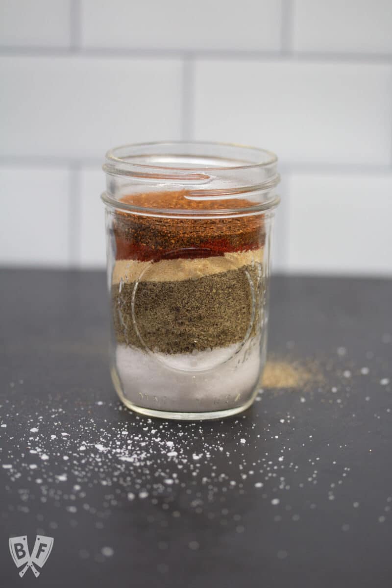 Spices for homemade grill seasoning layered in a glass jar.