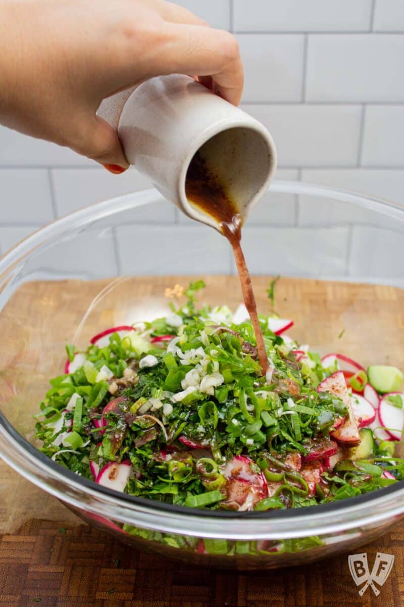 Pouring sumac vinaigrette over a fattoush salad.