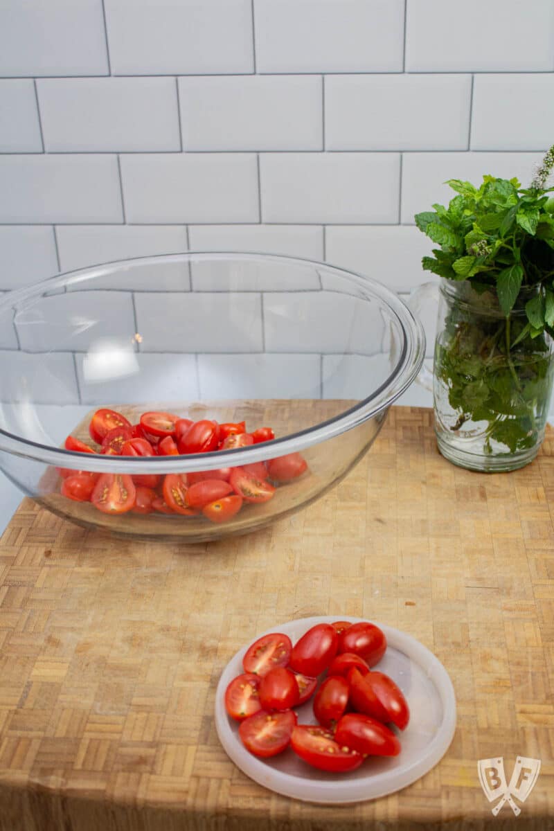 A bowl with sliced tomatoes and a glass of fresh herbs.