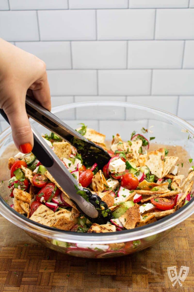 Tossing together ingredients for fattoush salad in a bowl.