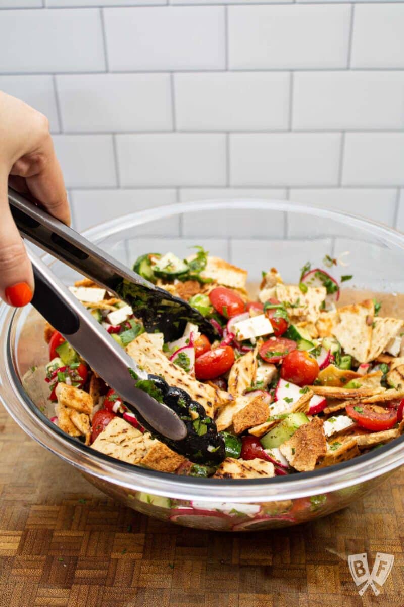 Tossing a bowl of fattoush salad together with tongs.