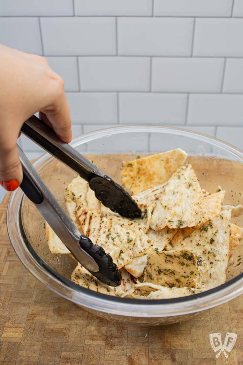 Using tongs to toss pita triangles with seasoned oil.